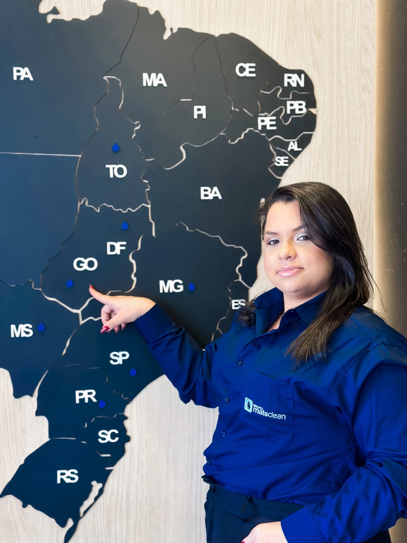 Colaboradora do Grupo Mais Clean apontando Goiás num mapa do Brasil com as cidades atendidas marcadas